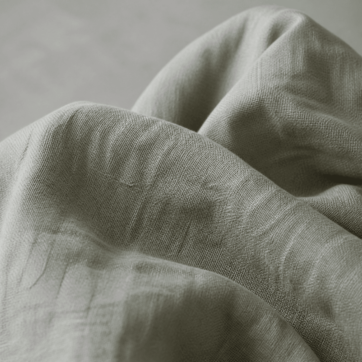 Macro view of softened sage-grey washed linen with relaxed natural creases